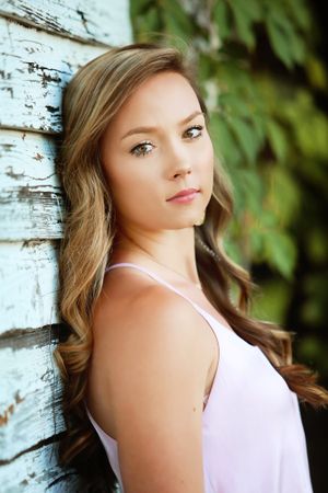 A soft portrait featuring a white summer dress against weathered white wood and green foliage.