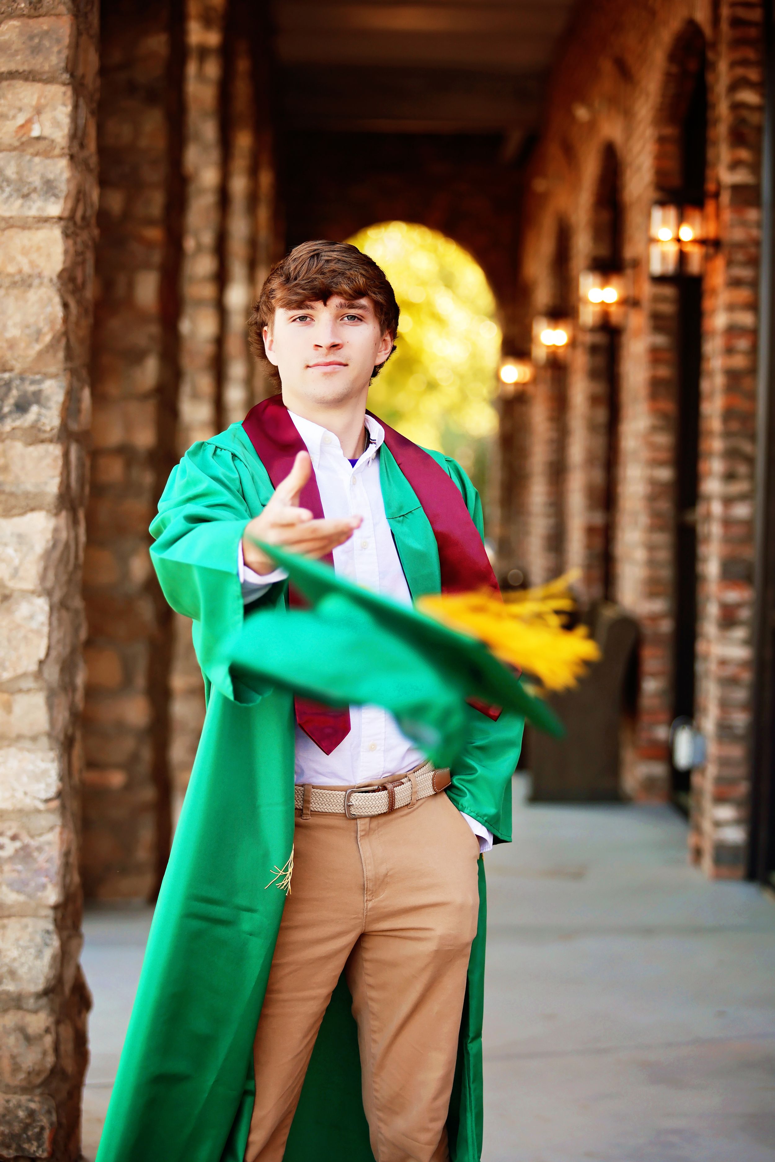 Person in bright green coat and khaki pants poses playfully in stone archway corridor with warm lighting.