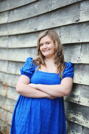Portrait of person in blue puff sleeve dress against weathered wooden wall.