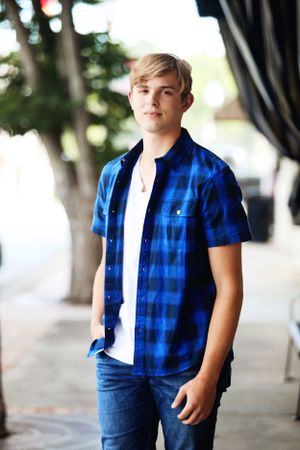 Casual portrait of teenager in blue plaid shirt standing outdoors.