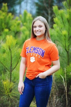 Student wearing orange Clemson Tigers t-shirt poses among pine trees.
