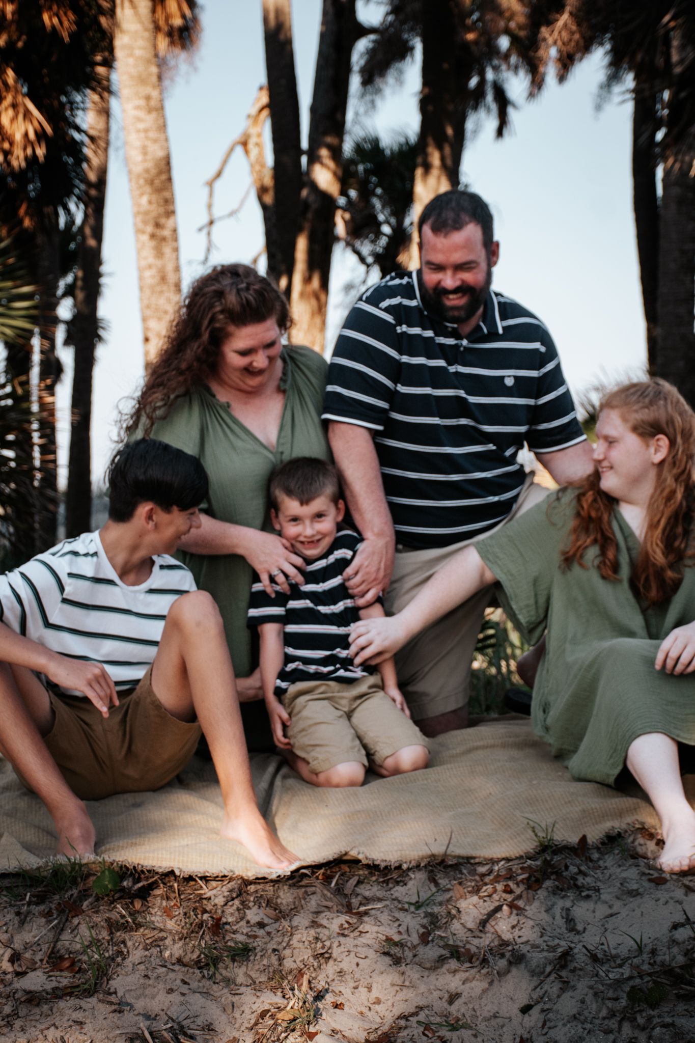 A happy group sitting together on sandy ground near palm trees at sunset.