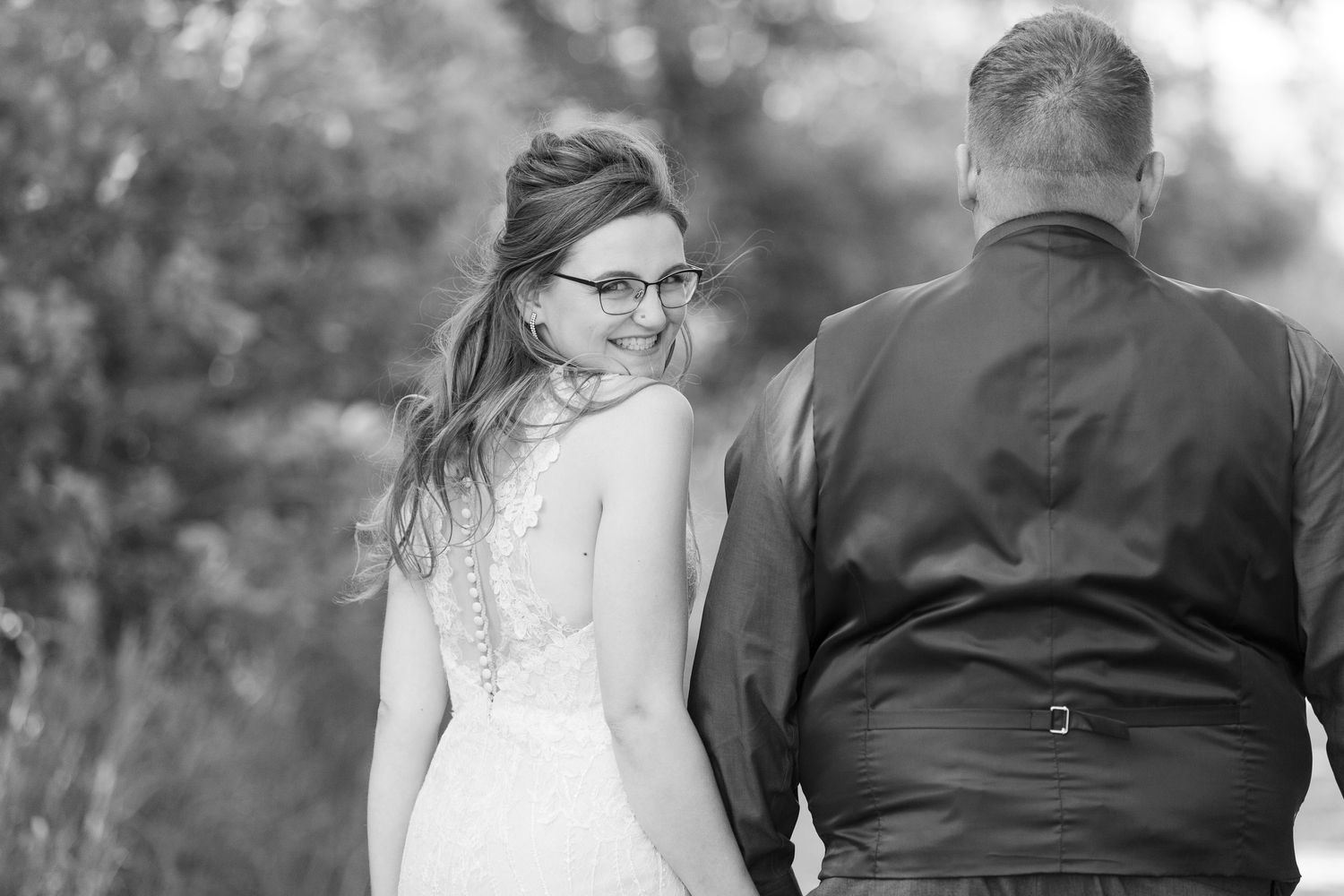 Black and white wedding portrait showing back of couple outdoors.