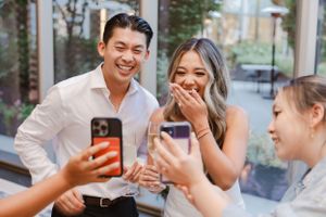 Group celebrating with phones capturing special moments by large windows.