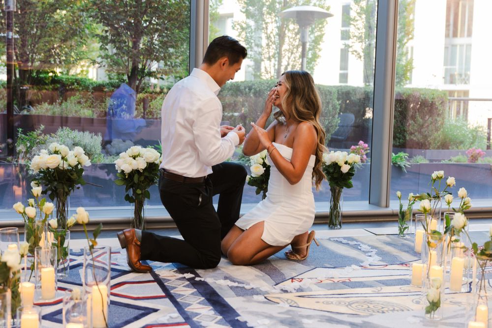 Romantic proposal scene with white floral arrangements in a sunlit indoor setting.