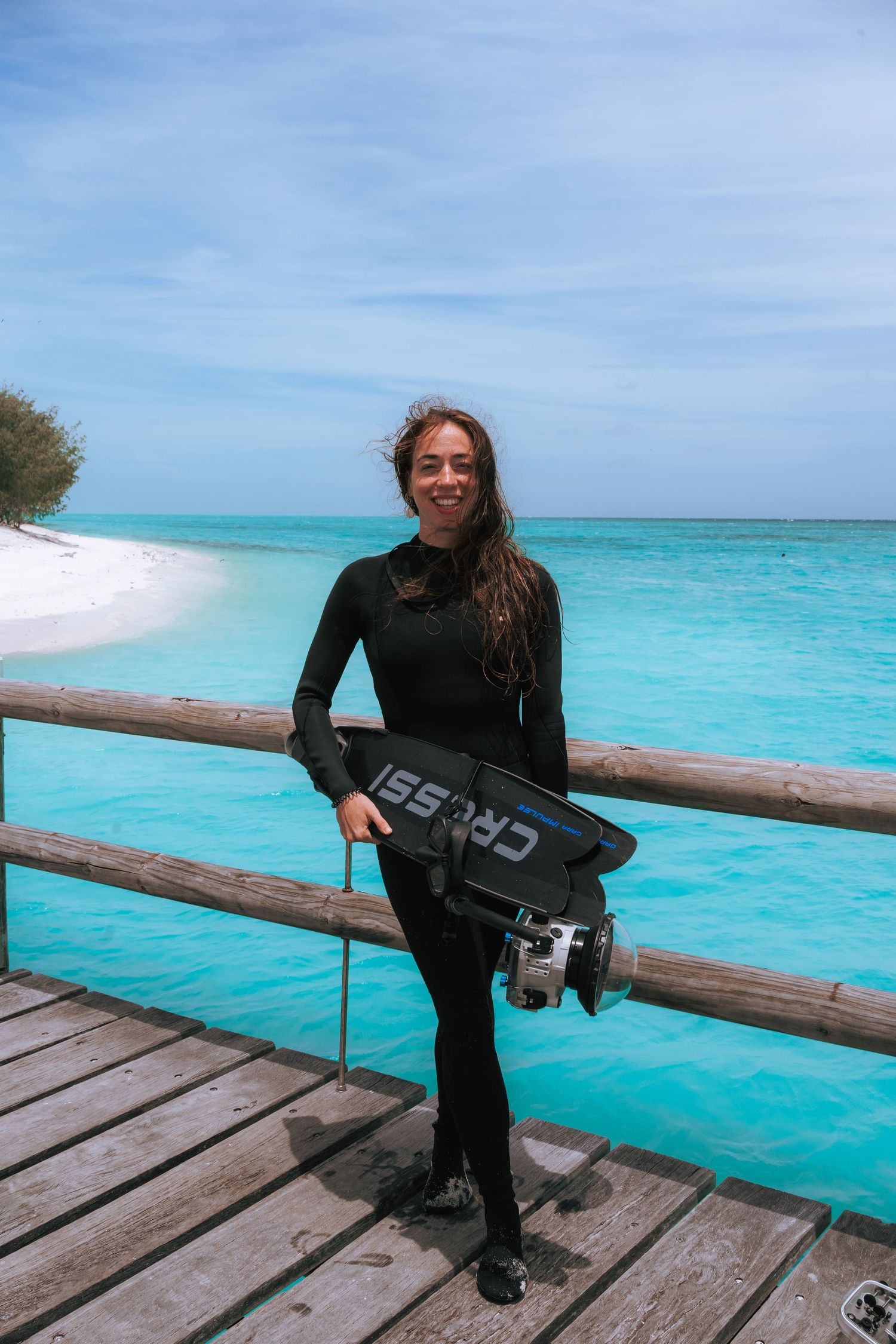 Gaby Salvador in wetsuit holding her diving gear and underwater camera setup on Heron Island's wooden pier.