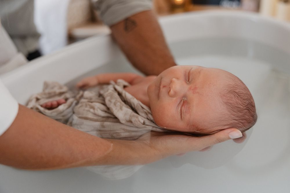 Photographe naissance a Lille, immortalisant un moment de bien-etre pour un bebe lors d’un bain de Sonia : bebe serein berce par ses parents