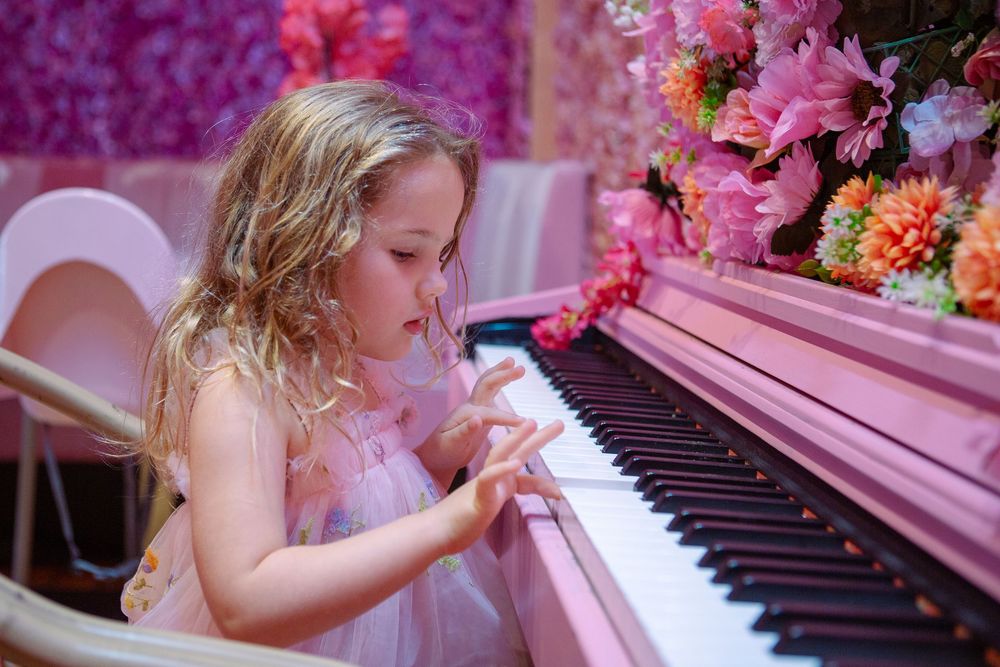 A pink piano sits among vibrant flowers creating a whimsical musical garden setting.