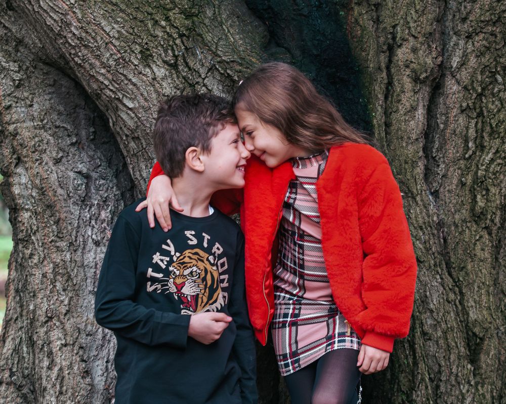 Two children sharing an intimate moment while leaning against large tree trunk.