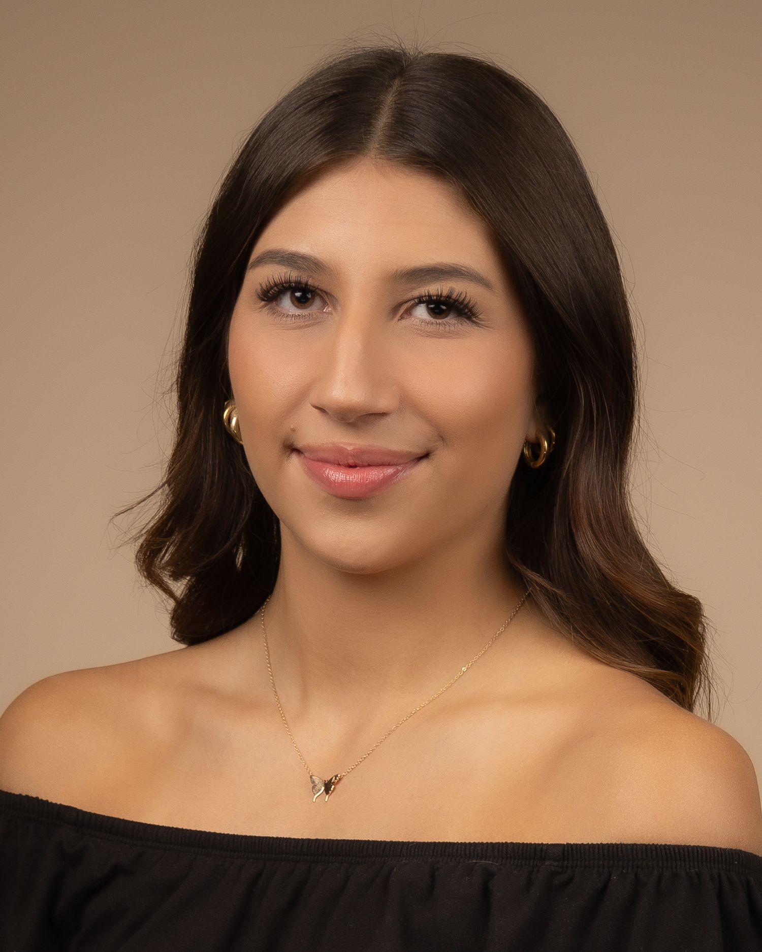 Portrait of a woman with wavy dark hair wearing an off-shoulder black top against a brown background.