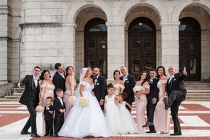 Large wedding party posing on steps of grand building with bride in ball gown and groom.