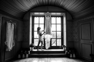 Black and white silhouette of woman admiring wedding dress hanging in arched window.