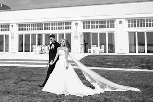 Black and white portrait of bride and groom on lawn before elegant white building.