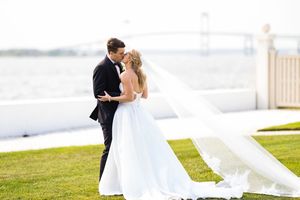Bride and groom sharing a romantic kiss outdoors near a waterfront bridge on their wedding day.