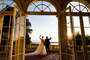 Bride and groom silhouetted in elegant French doors at sunset overlooking a scenic waterfront venue.