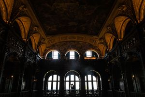Dramatic dark interior of an ornate historic hall with arched windows and painted ceiling.