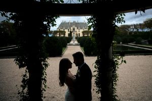 Romantic silhouette of bride and groom facing each other beneath a garden arbor at a chateau.