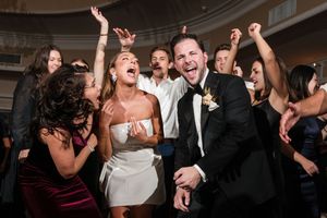 Joyful bride and groom celebrate with guests on the dance floor at lively wedding reception party.