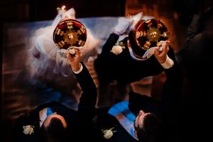 Overhead view of bride and groom holding glowing amber cocktail glasses at atmospheric wedding reception.