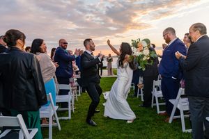 Newlyweds joyfully walk back down the aisle after outdoor wedding ceremony at a stunning sunset venue.