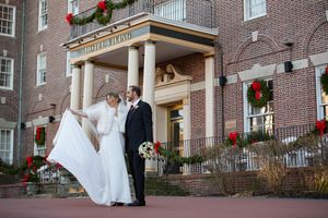 Bride and groom pose outside a historic hotel decorated with festive Christmas wreaths in winter.