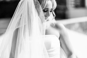 Elegant bride in a white strapless gown and veil poses in a soft black and white portrait.