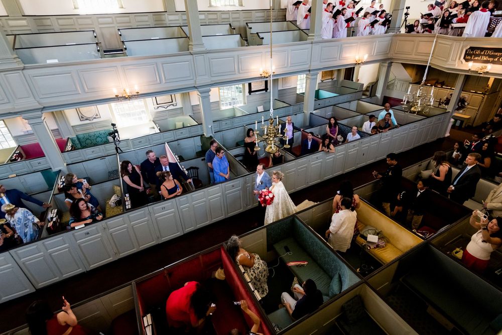 Aerial view of a bride and groom walking down the aisle of a historic church filled with guests.