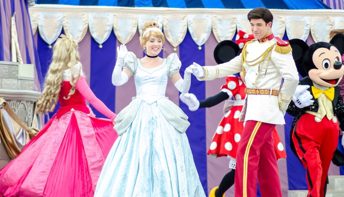 Disney characters in colorful costumes performing on stage with flowing dresses and props.