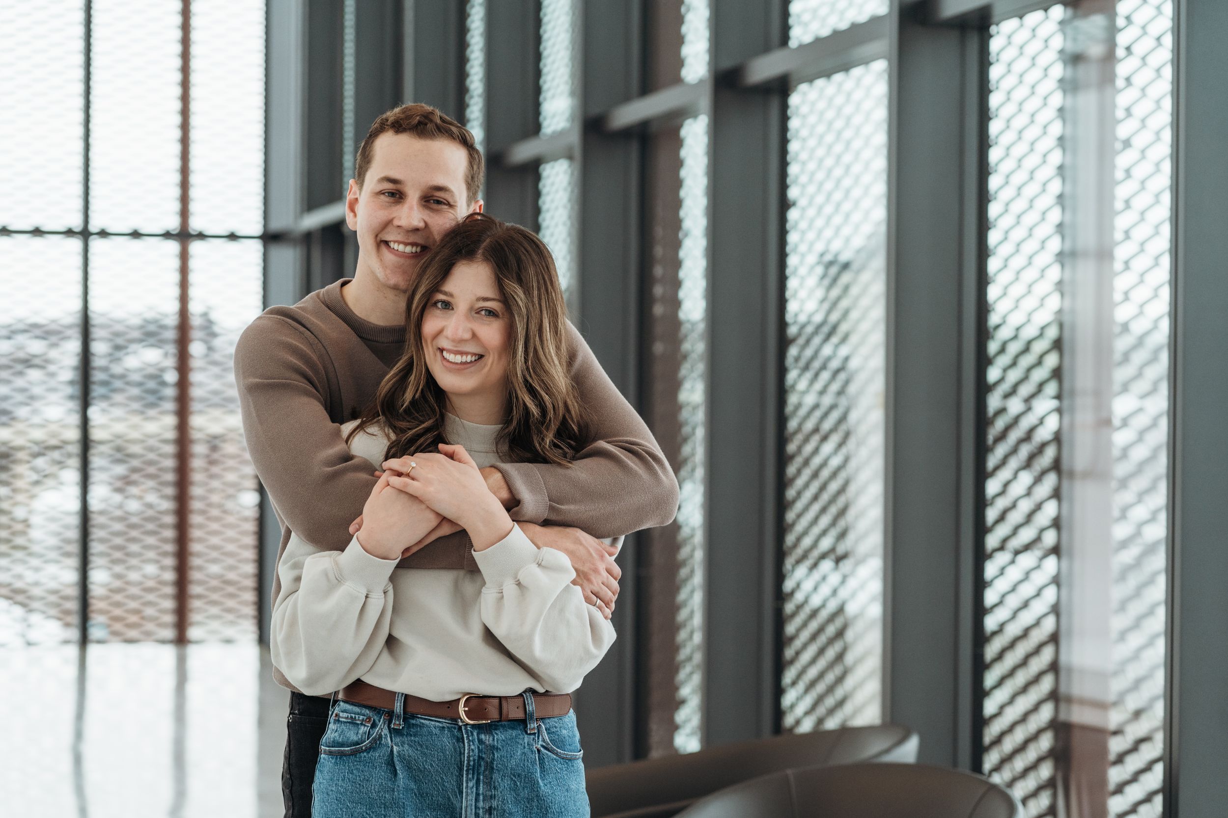 Two people embrace and laugh together in a modern interior space.