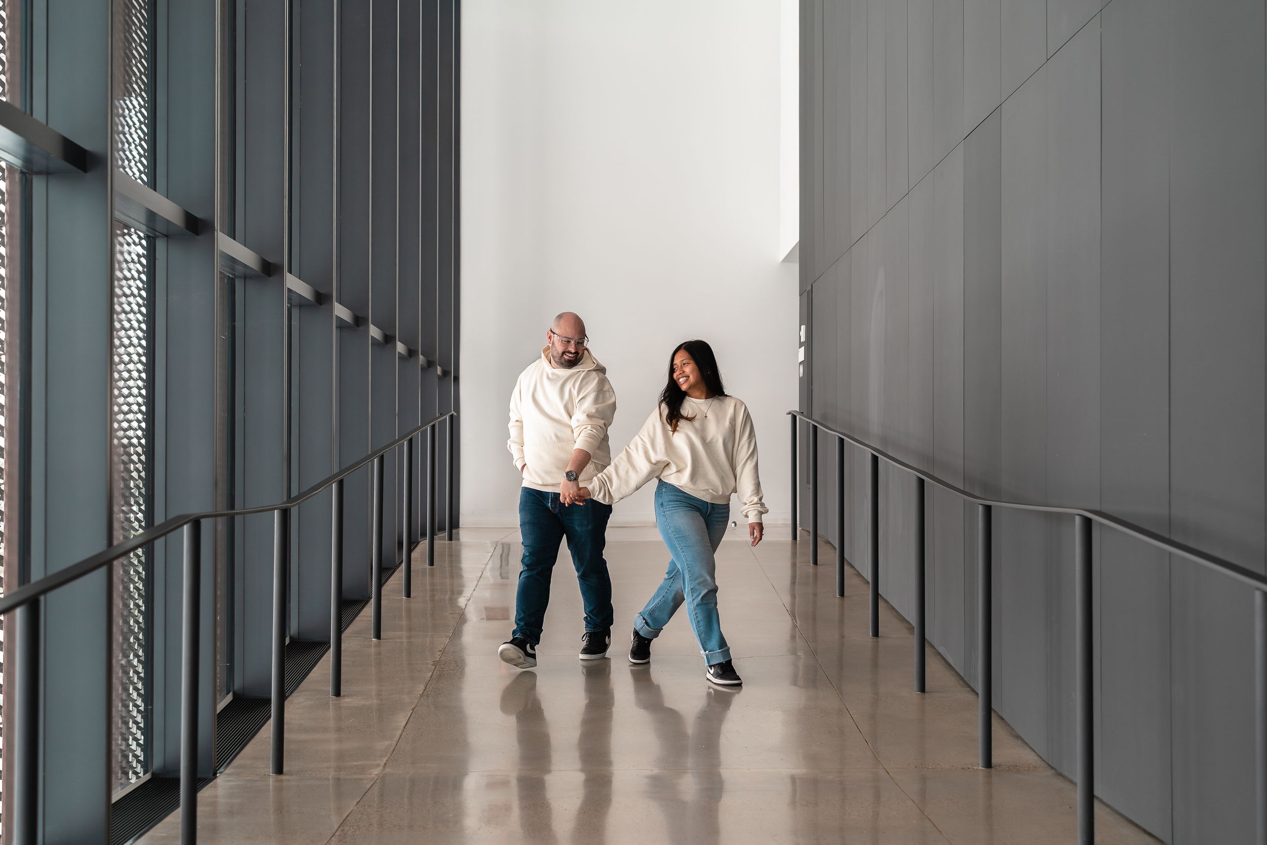 People walk and interact in a modern architectural hallway with tall gray walls and metallic design elements.