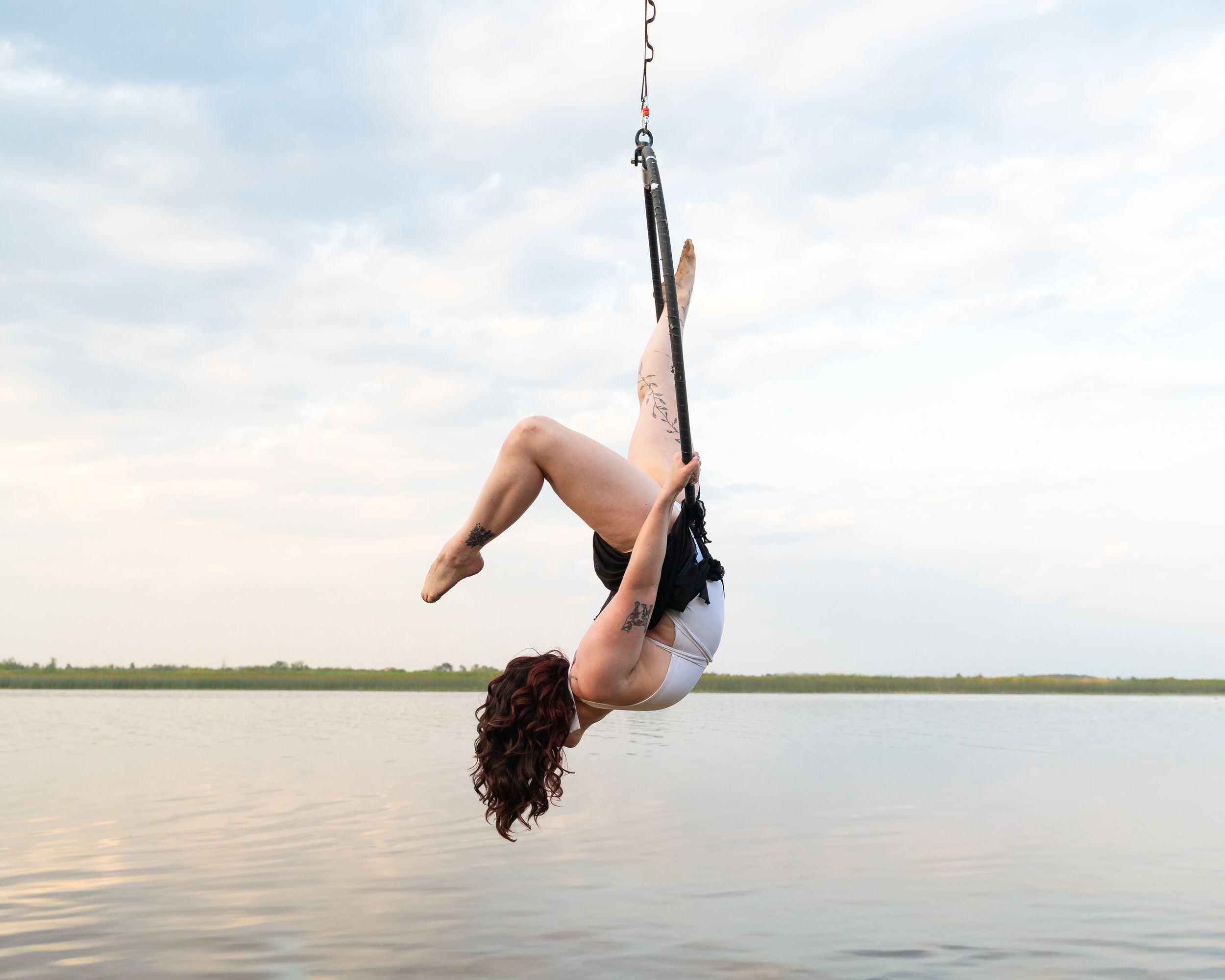 A person flips backwards off a boat into a tranquil lake against an overcast sky.