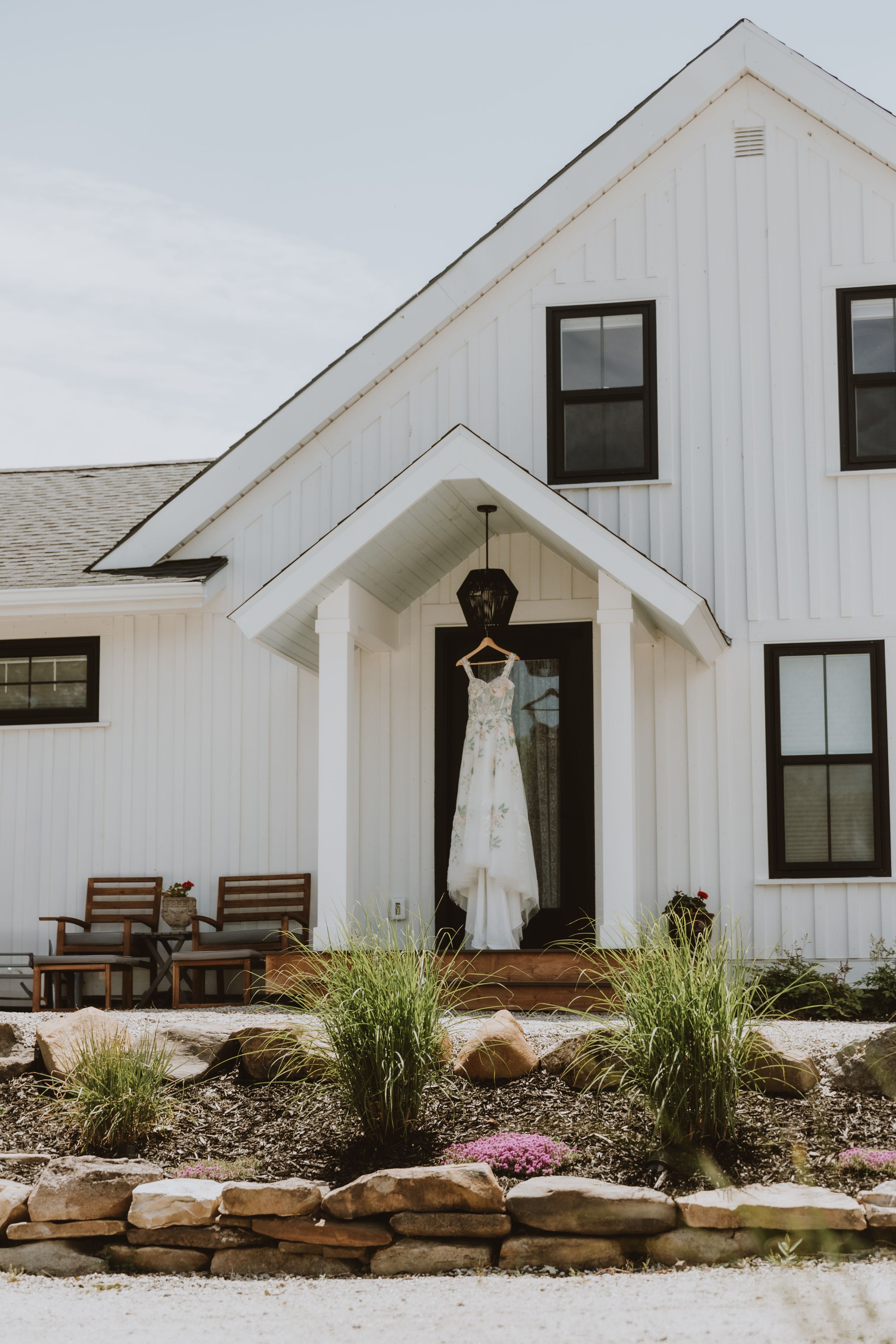 White farmhouse style building with black trim windows and a hanging wedding dress displayed in the front entrance.