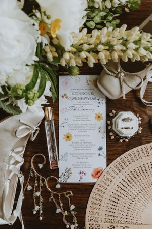 Wedding invitation flatlay with floral design menu card, decorative fan, white ribbon and delicate flower arrangements.