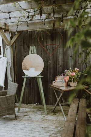 Cozy outdoor patio with vintage decor, white chair, and green plant stand against rustic wooden fence with string lights.
