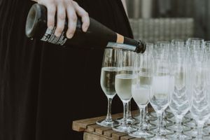 Someone pouring champagne into elegant flute glasses arranged on a wooden tray.