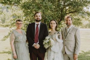 Wedding party poses together outdoors in sunlit natural setting with bouquet and formal attire.