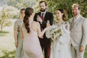 A joyful outdoor wedding ceremony in warm sunlight with the couple, officiant and wedding party sharing a lighthearted moment.