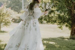 A ethereal wedding dress with delicate floral embroidery flows in a dreamy outdoor garden setting.