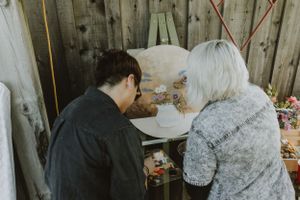 Two people sitting together at a rustic wooden table examining something indoors.