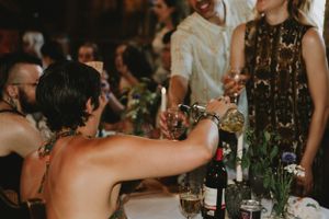 Wedding reception scene with guests raising glasses for a toast at a decorated dinner table.