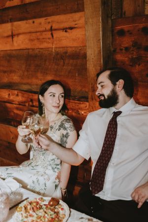 Wedding reception celebration with couple toasting wine glasses in rustic wooden venue.