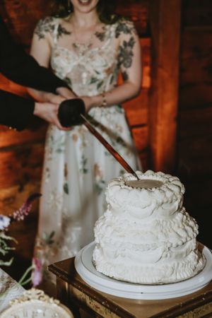Three-tiered white wedding cake with textured frosting being cut during reception.