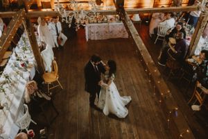 Overhead view of a rustic barn wedding reception with string lights and couples dancing on wooden floors.