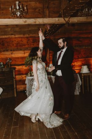 Couple dancing in rustic barn venue with string lights and wooden walls.