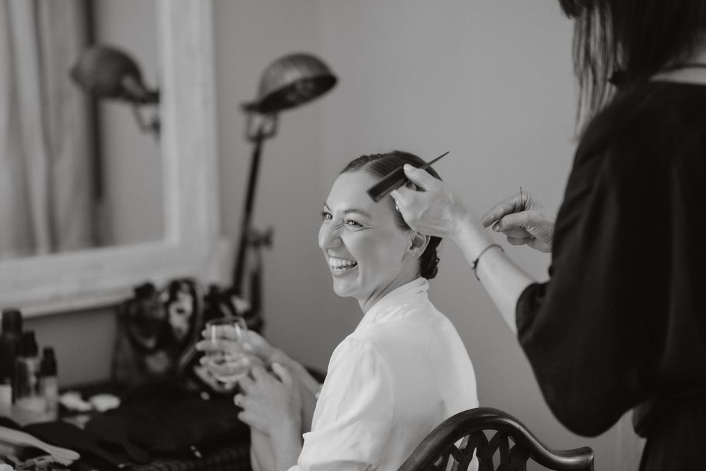 Black and white image showing a person getting their hair styled while sitting in a salon chair with a happy expression.