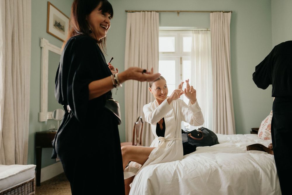 Two people interact joyfully while getting ready in a bright hotel room with white curtains and bedding.
