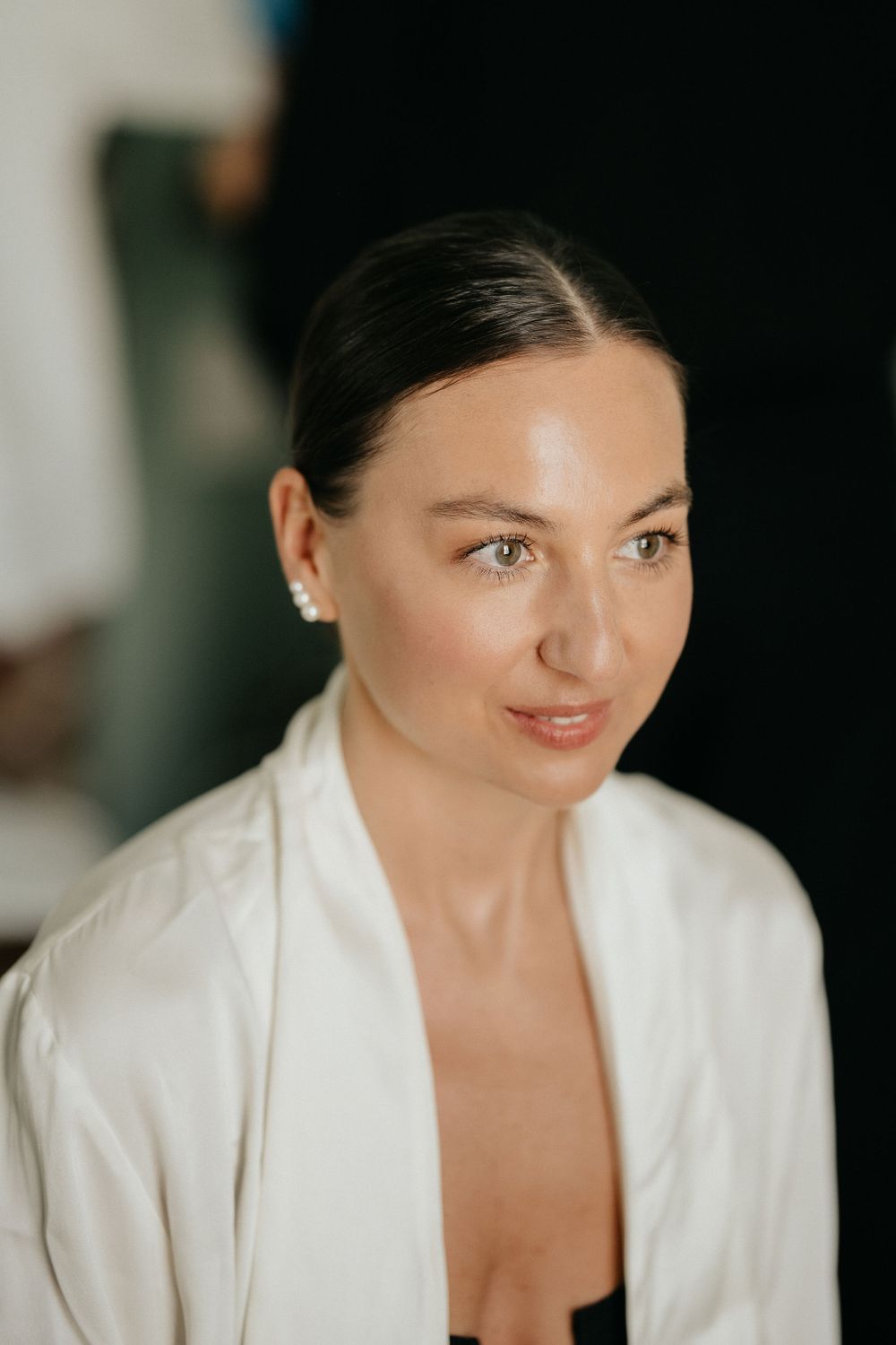 A woman in a white robe smiles softly at the camera while wearing subtle makeup and natural lighting.
