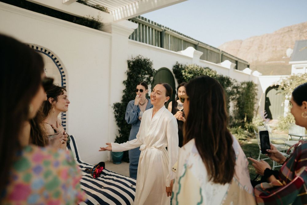 A social gathering on a bright patio with guests mingling near white walls and decorative outdoor furnishings.