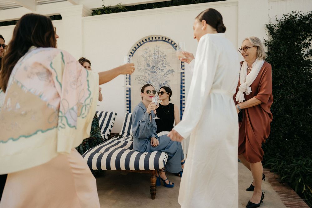People gather around a decorative striped loveseat at an outdoor event with greenery in the background.
