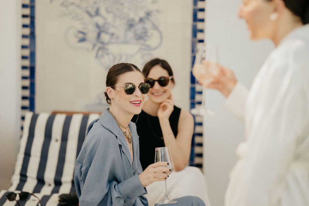 Friends relaxing outdoors with drinks on a sunny day near blue and white striped cushions.
